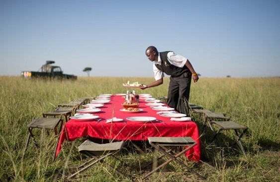Hot Air Balloon Safari Masai Mara 4 Hot air balloon safari Masai Mara for couples — couple sharing champagne at bush breakfast table with balloon envelope behind them on the Mara plains at sunrise
