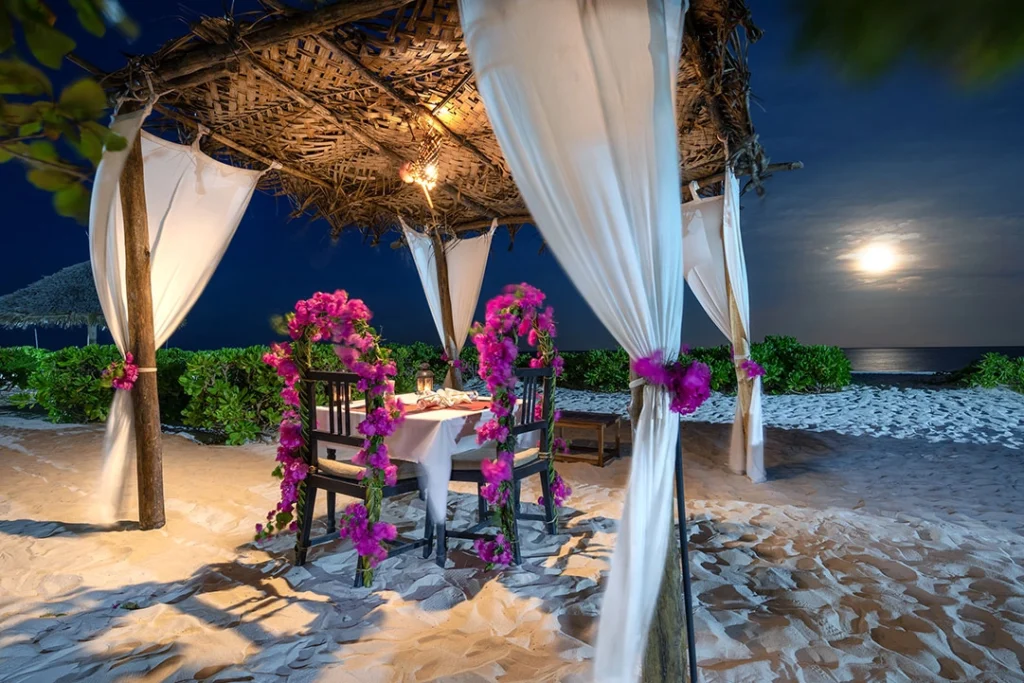 Zanzibar Beach Holidays 15 Romantic Zanzibar beach dinner setup with candles, table for two on white sand, ocean sunset background, perfect honeymoon experience.